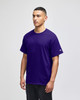 A purple Champion short-sleeve T-shirt worn by a model standing against a plain background. It features a logo on the sleeve.