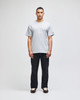 A grey short-sleeve t-shirt worn by a model, paired with dark pants. The shirt has a small logo on the sleeve.