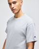 A grey short-sleeve t-shirt featuring a branded logo on the sleeve, displayed by a model.