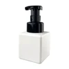 A square white foaming soap dispenser with a black pump top. Features a logo on the front.