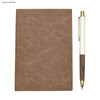 A brown notebook with a textured cover and a white pen with a wooden design, featuring a logo.