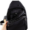 A black sling bag is shown, featuring multiple zippered pockets and a hand holding it open to display the interior.