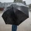 A black umbrella in heavy rain, held by a person wearing blue jeans, with raindrops falling around it.