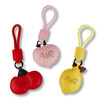 Three bag charms in red, pink, and yellow, featuring apple and lemon shapes with one charm having a logo.