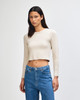 A fitted long-sleeve crop t-shirt in a light beige colour, paired with blue jeans. The model is standing and looking directly at the camera.