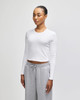 A white long-sleeve crop fitted T-shirt, modelled by a woman, paired with grey sweatpants. The shirt features a logo.