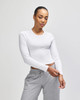 A fitted white long-sleeve cropped T-shirt worn with grey sweatpants, featuring a logo on the shirt.