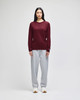 A long-sleeve t-shirt in maroon worn with grey sweatpants. The t-shirt features a logo on the sleeve.