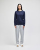 A long-sleeve navy T-shirt displayed on a model paired with grey sweatpants and white sneakers. The shirt features a logo.