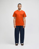 An orange short-sleeve t-shirt worn by a man, paired with navy blue pants, displaying a logo on the shirt.