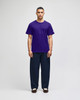A model wearing a purple Champion adult jersey short sleeve t-shirt and dark blue pants, featuring a logo.
