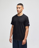 A black short sleeve t-shirt with a logo on the sleeve, displayed by a model standing against a neutral background.