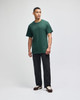 A green short sleeve t-shirt worn by a standing man, paired with dark pants and shoes. The shirt has a logo.