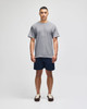 A model wearing a grey short sleeve t-shirt and navy shorts, featuring a logo on the t-shirt.