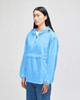 A blue packable anorak jacket with a half-zip and hood, featuring a logo on the sleeve.