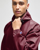 A maroon packable anorak jacket featuring a hood and adjustable cuffs, with a logo on the sleeve.