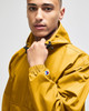 A packable anorak jacket in mustard yellow, featuring a hood and an adjustable neckline. It has a logo on the sleeve.