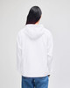 A white packable anorak jacket with a hood, viewed from the back, worn over blue jeans. The jacket features a logo.