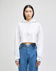 A white cropped hoodie with a hood, featuring long sleeves, paired with blue jeans, and includes a logo.