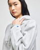 A grey cropped hoodie with a large hood and a logo on the sleeve, modelled by a woman.