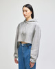 A cropped hoodie in grey, featuring a hood and drawstrings, displayed on a model wearing blue jeans.