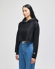 A black cropped hoodie with a hood, featuring long sleeves and a logo. Worn with blue jeans.