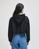 A black cropped hoodie with a hood, worn by a person facing away, paired with blue jeans.