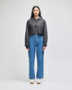 A model wears a grey cropped hoodie and loose blue jeans, paired with white sneakers, with a plain background.