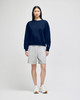 A navy crewneck sweatshirt worn with grey shorts and white sneakers, featuring a logo on the sweatshirt.