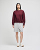 A burgundy crewneck sweatshirt paired with grey shorts on a model, with white sneakers. The sweatshirt features a logo.