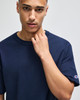 A navy blue Champion Adult Heritage Jersey T-Shirt featuring a logo on the sleeve, held by a model.