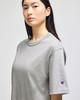 A grey Champion Adult Heritage Jersey T-Shirt is displayed on a model, featuring a logo on one sleeve.
