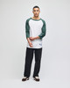 A raglan baseball T-shirt in white with green sleeves, paired with black pants. It features a logo on the hem.
