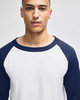 A man wearing a white and navy raglan baseball t-shirt paired with dark pants. The shirt has a logo.