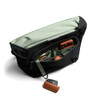 A black messenger bag with a green interior and multiple compartments, holding devices and accessories.