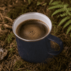 A drink bottle featuring a navy blue mug filled with dark coffee, set on a natural, forested background.