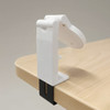 A white mobile phone stand clamps onto a wooden surface, featuring an adjustable holder for the device.