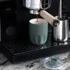 A drink bottle in a muted green colour with a ceramic liner, placed near an espresso machine on a black countertop.