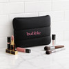 A black neoprene cosmetic bag with pink branding, surrounded by various lip products and makeup brushes.