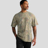 A man wearing a heavy faded camo T-shirt in shades of green and brown, featuring short sleeves and a relaxed fit.