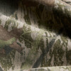 A close-up of fabric featuring a heavy faded camo pattern in green and brown tones.