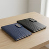 Two Nexus Notebooks in navy and black, each featuring a textured cover and a branding logo, resting on a wooden table.