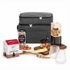 A grey insulated bag filled with gourmet snacks, including biscuits, sweets, and a wooden cheese board with utensils.