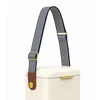 A cooler with a cream body features a navy and white striped shoulder strap and a brown leather accent.