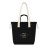 A black tote bag with long beige handles and a front pocket featuring a logo.