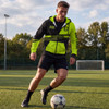 A man wearing a vibrant yellow and black active zipped hoodie dribbles a soccer ball on a grassy field.