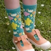 Jolly knitted bamboo kids' socks in teal with colourful floral patterns, worn with light-coloured shoes on grass.