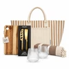 A striped tote bag, a wooden cheese board, a cheese knife set, two clear glasses, and a patterned blanket.
