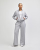 A woman stands in a light grey full-zip jacket paired with matching wide-leg pants. The jacket has a logo.