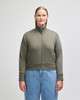 A women's full-zip jacket in olive green, featuring a high collar and ribbed cuffs, with a logo visible.